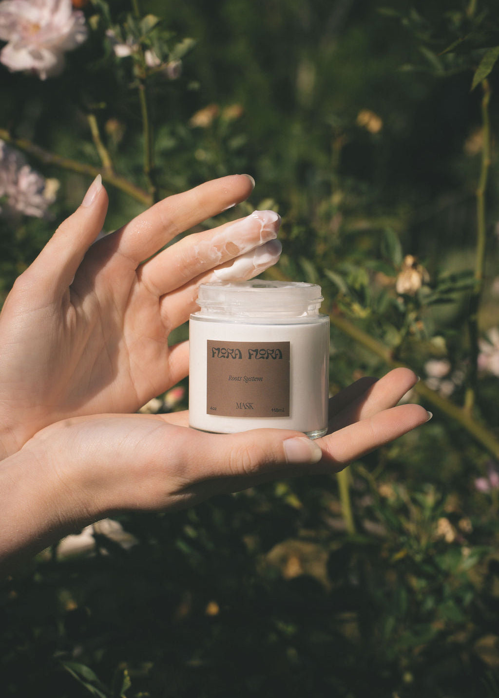 Hand holding a jar of root systems hair mask with a natural background
