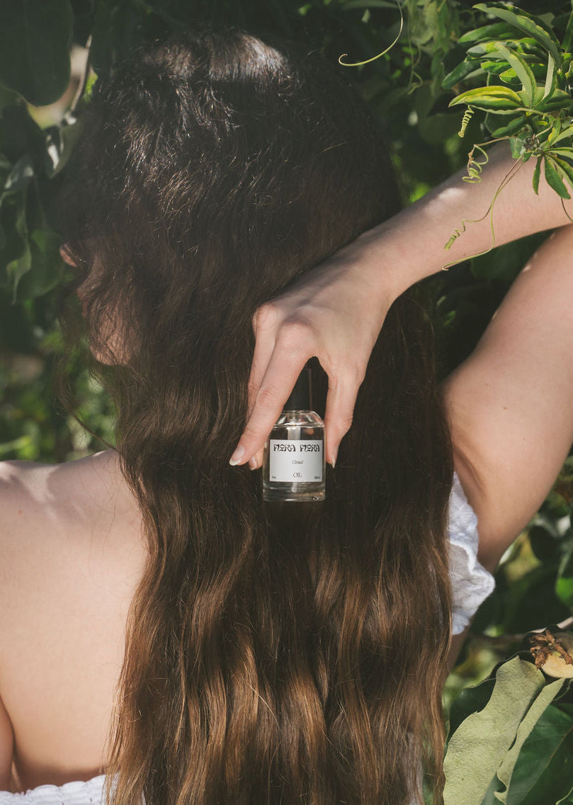 Woman holding a bottle of cloud hair oil with greenery in the background